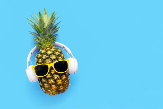 Ripe pineapple with sunglasses and headphones on blue background. Copy space