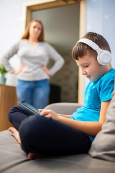 Mother scolds her son. Boy uses tablet computer with headphones and ignores his mom. Family relationships concept