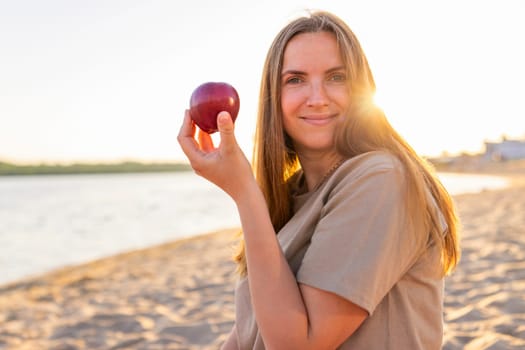 Portrait of young beautiful smiling woman with apple on sea beach.