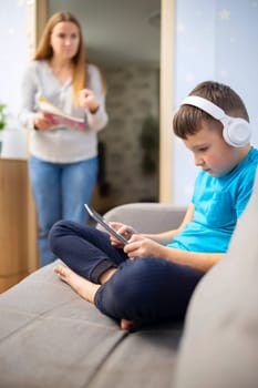 Mother scolds her son. Boy uses tablet computer with headphones and ignores his mom. Family relationships concept