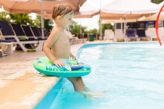 Child in swimming pool with inflatable circle enjoys summer vacation. A happy kid playing in the pool