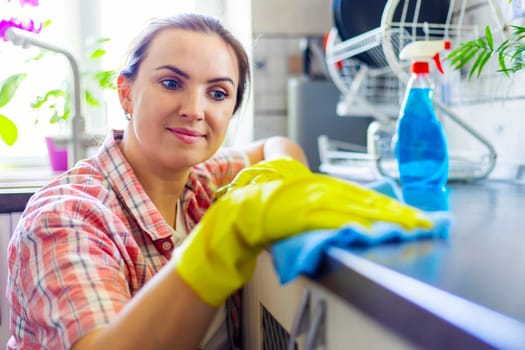 Housewife in yellow gloves wipes dust using spray detergent and rag. The woman is doing household chores. Cleaning concept