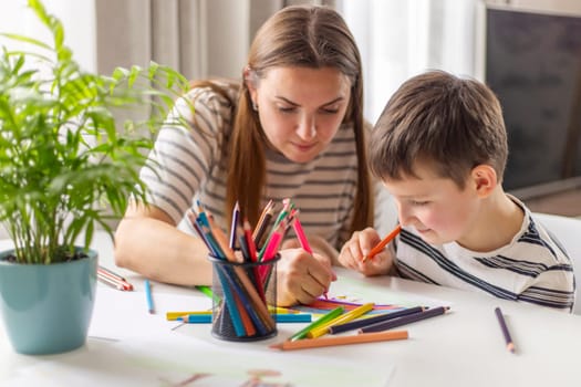 Mother and child drawing with pencils sitting at the desk at home. Happy family