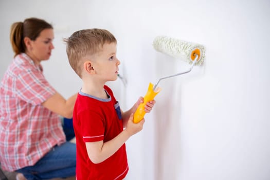 Happy family mother and child son paint the wall with paint using roller and brush. Repair in the apartment