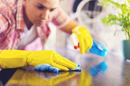 Housewife in yellow gloves wipes dust using spray detergent and rag. The woman is doing household chores. Cleaning concept