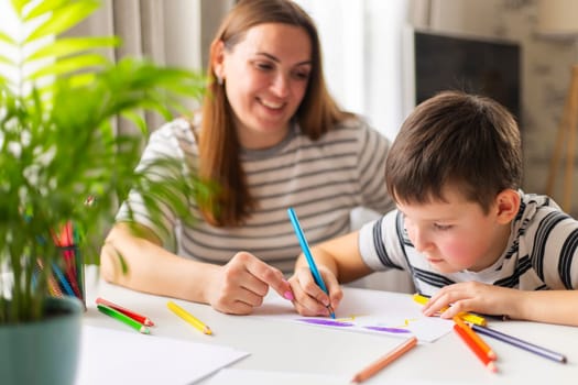 Mother and child drawing with pencils sitting at the desk at home. Happy family