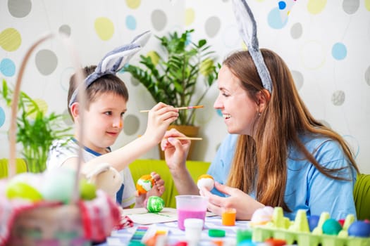 Happy Easter. A mother and her son painting Easter eggs. Happy family getting ready for Easter. Mom and child boy wearing bunny ears on Easter day