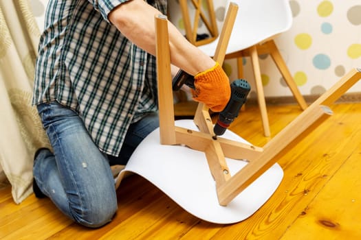 Assemble the furniture. A man assembling a chair. Furniture assembler with a drill. Craftsman with tools to repair a chair