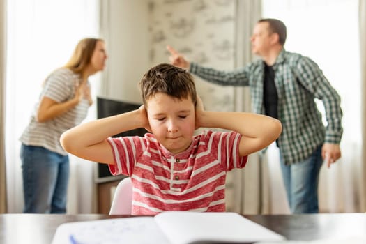 A sad child covers his ears with his hands during an argument between his parents. Family conflicts or divorce impact on on child development