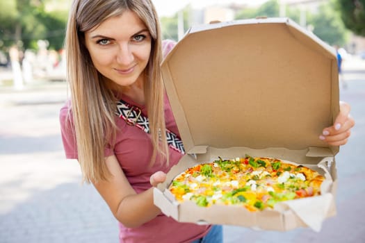 Woman holding box of takeaway pizza in her hands outdoor.