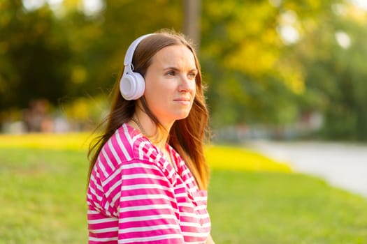 Relaxed woman sitting on the grass listening to music with headphones in a park on sunny summer day