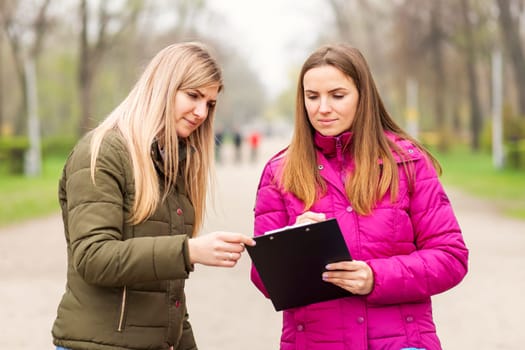 Opinion poll. A woman interviewing people, conducting survey standing outdoor.