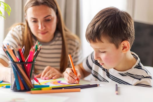 Mother and child drawing with pencils sitting at the desk at home. Happy family