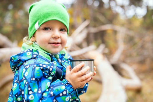 Little cute boy drinks hot tea from a thermos in the park. Child drinking hot tea outdoors