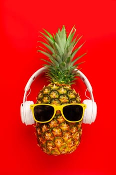 Ripe pineapple with sunglasses and headphones on red background. Copy space