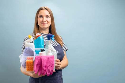 Woman housewife or maid holding a container with a set of cleaning products on blue background
