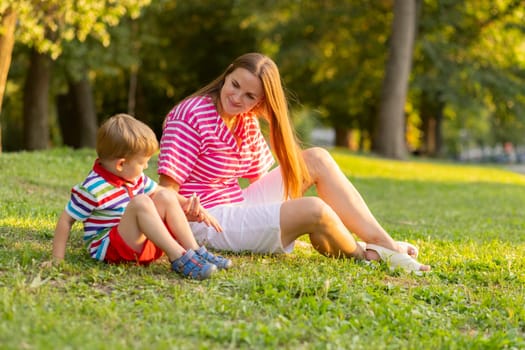 Mother having rest with her little kid son together outdoors in park. Love family concept