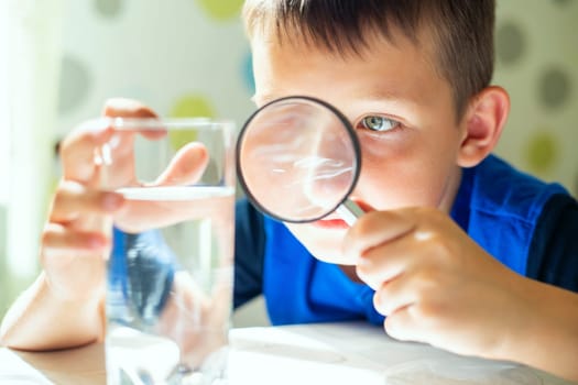 The child boy looking at water in a glass through magnifying glass. Water quality check concept.