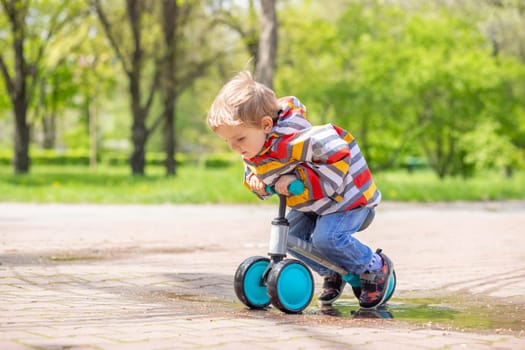 Active blond boy riding balance bike or run bike outdoor park. Active kid playing outside