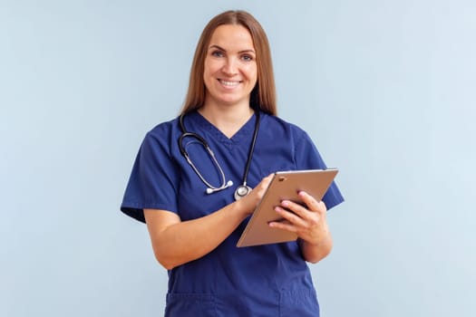 Smiling young woman doctor work on tablet on blue background. Modern device for remote online consultation, social distance and new normal with new medical application