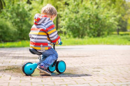 Active blond boy riding balance bike or run bike outdoor park. Active kid playing outside