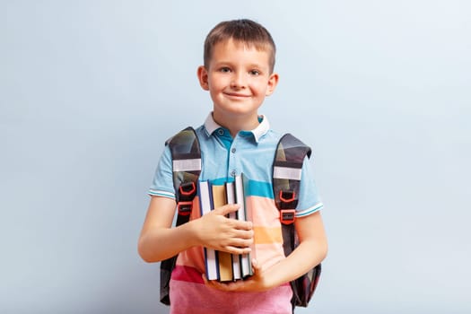 Cute school boy with backpack holding books on blue background for education concept.