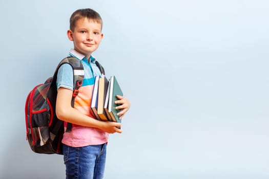 Cute school boy with backpack holding books on blue background for education concept.