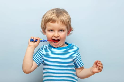 Little blonde boy brushing teeth with toothbrush on blue background. Dental hygiene.
