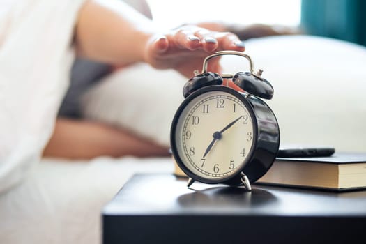 Young sleeping woman on the bed reaches her hand to turn off the alarm clock wakes up in the morning