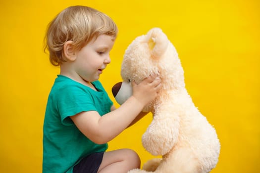 Little boy hugging teddy bear toy on yellow background.