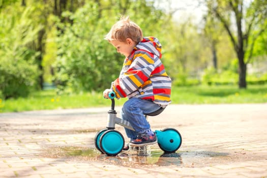 Active blond boy riding balance bike or run bike outdoor park. Active kid playing outside