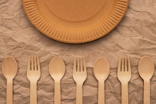 Wooden forks and spoons and paper plate on crumpled paper. Biodegradable eco-friendly dishes