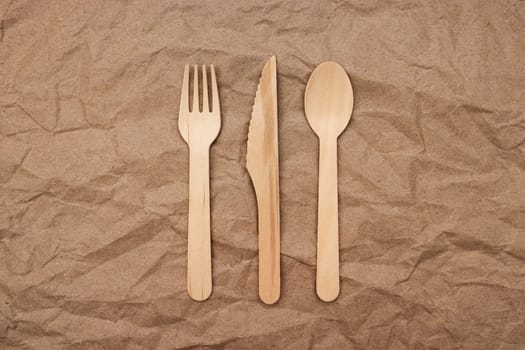 Wooden fork, spoon and knife on crumpled paper background. Biodegradable eco-friendly dishes. Top view