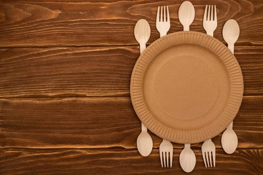 Wooden forks and spoons and paper plate on wooden background. Biodegradable eco-friendly dishes