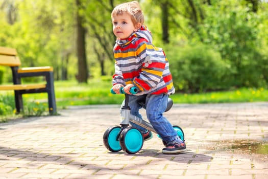 Active blond boy riding balance bike or run bike outdoor park. Active kid playing outside