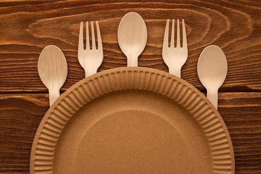 Wooden forks and spoons and paper plate on wooden background. Biodegradable eco-friendly dishes