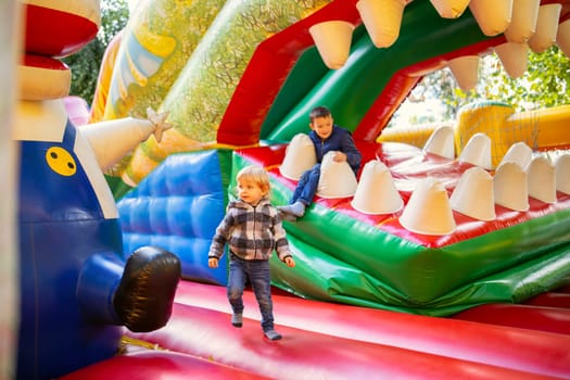 Happy kids having fun on colorful inflatable attraction playground. Children have fun and ride on the outdoor playground.