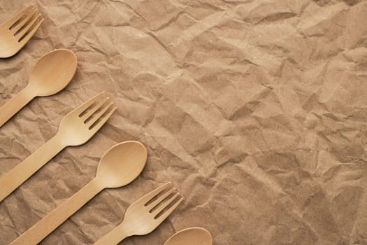 Set of wooden forks and spoons on crumpled paper background. Biodegradable eco-friendly dishes. Top view