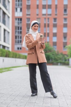 Young woman in hijab using smartphone outdoors