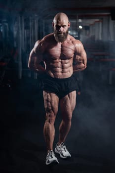 Muscular bald man posing in shorts. Bodybuilder showing off his shape in the gym