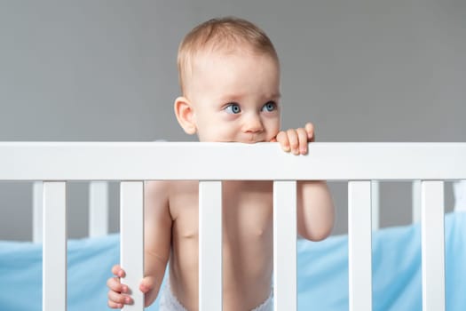 Happy baby playing in the crib, with a sweet smile, and gnawing on its side.