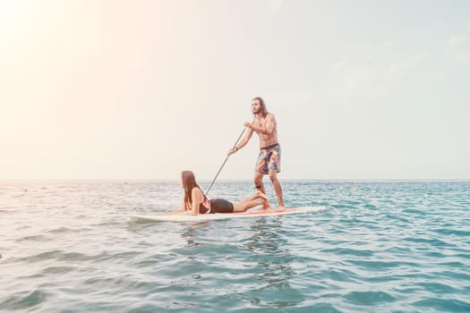 Sea woman and man on sup. Silhouette of happy young woman and man, surfing on SUP board, confident paddling through water surface. Idyllic sunset. Active lifestyle at sea or river