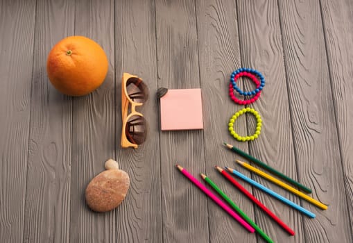 artist pencils for inscription. accessories sunscreen spf care. sunglasses bracelets orange fruit pebbles. Summer background template mockup space colorful composition text. Top view wooden background