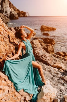 Woman green dress sea. Woman in a long mint dress posing on a beach with rocks on sunny day. Girl on the nature on blue sky background