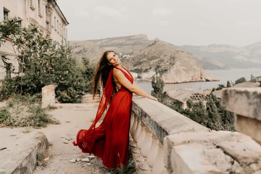 Woman red dress. Summer lifestyle of a happy woman posing near a fence with balusters over the sea