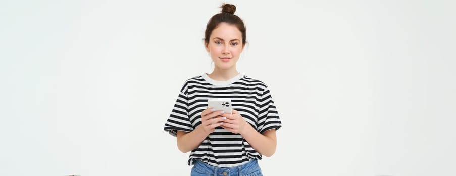 Technology and lifestyle. Young woman standing over white background with smartphone.