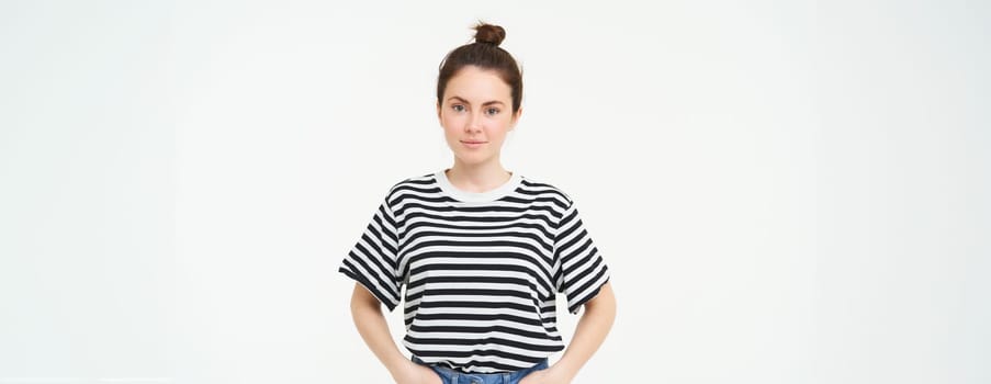 Image of young confident woman in casual outfit, looking happy, standing against white background.