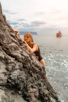 Woman travel sea. Attractive blonde woman in a black swimsuit enjoying the sea air on the seashore around the rocks. Travel and vacation concept