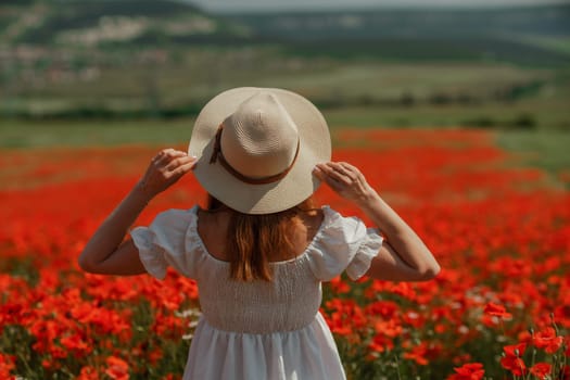 Field poppies woman. Happy woman in a white dress and hat stand through a blooming field of poppy raised her hands up. Field of blooming poppies