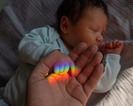 A man holds his newborn son's hand. Beam of light through a prism